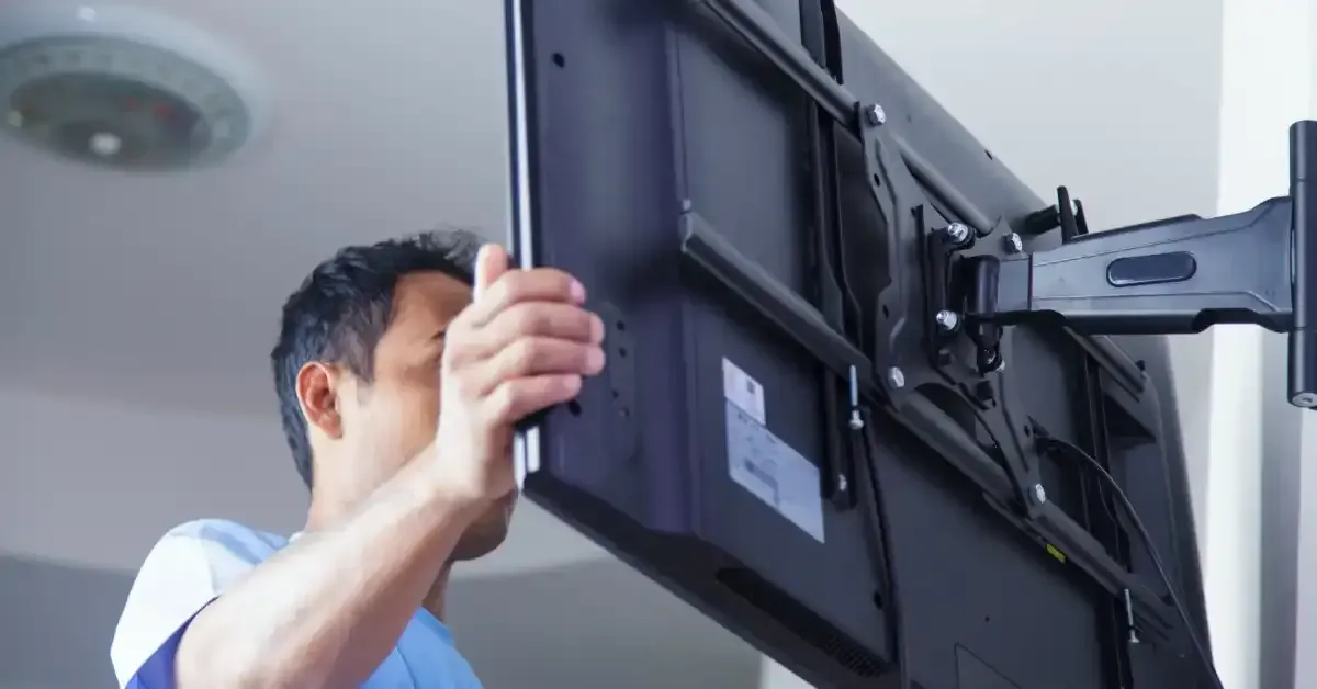 Man installing a large black television on a wall mount in a room.