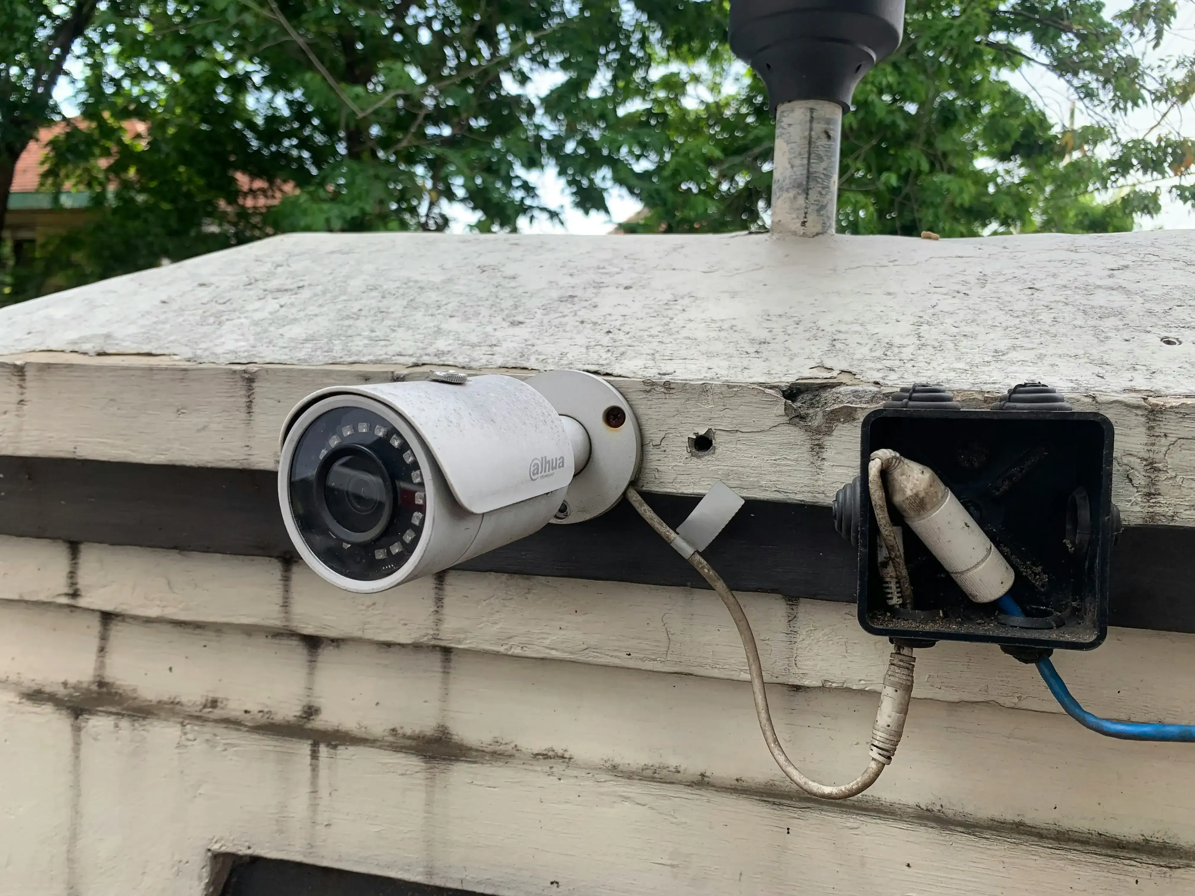 Security camera mounted on a white brick wall, next to an electrical box and a vent.