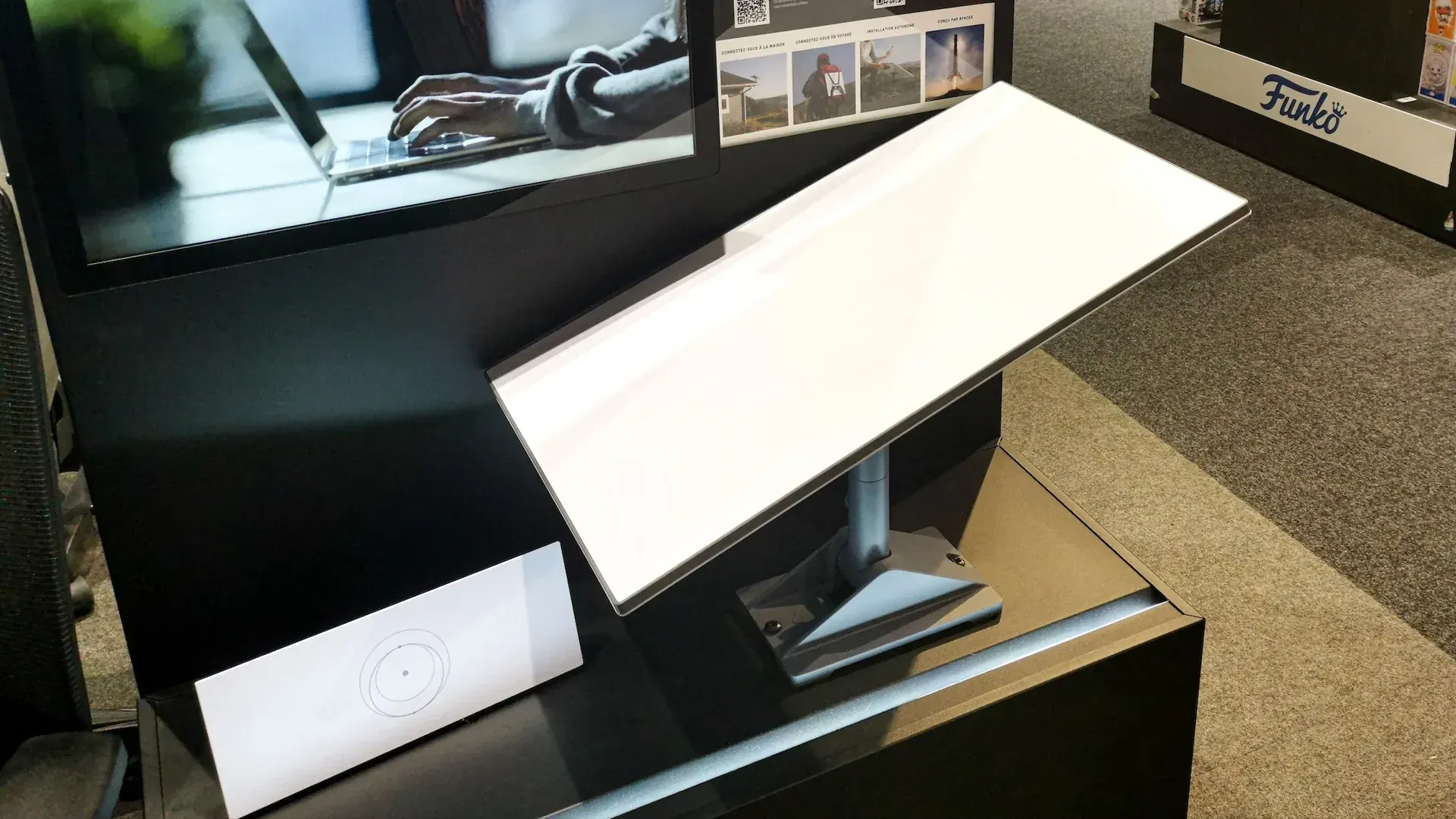 A white computer monitor angled on a display in a store, with a black desk and products in the background.