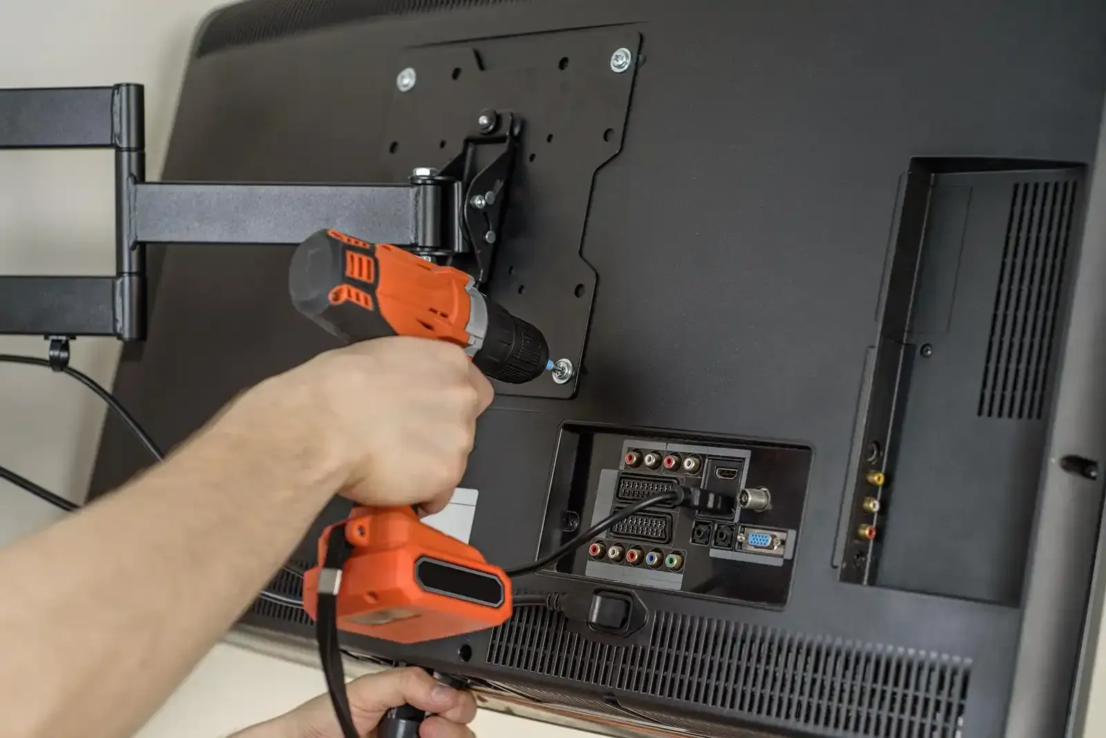 Person using a drill to attach a TV mount to the back of a large, black television.