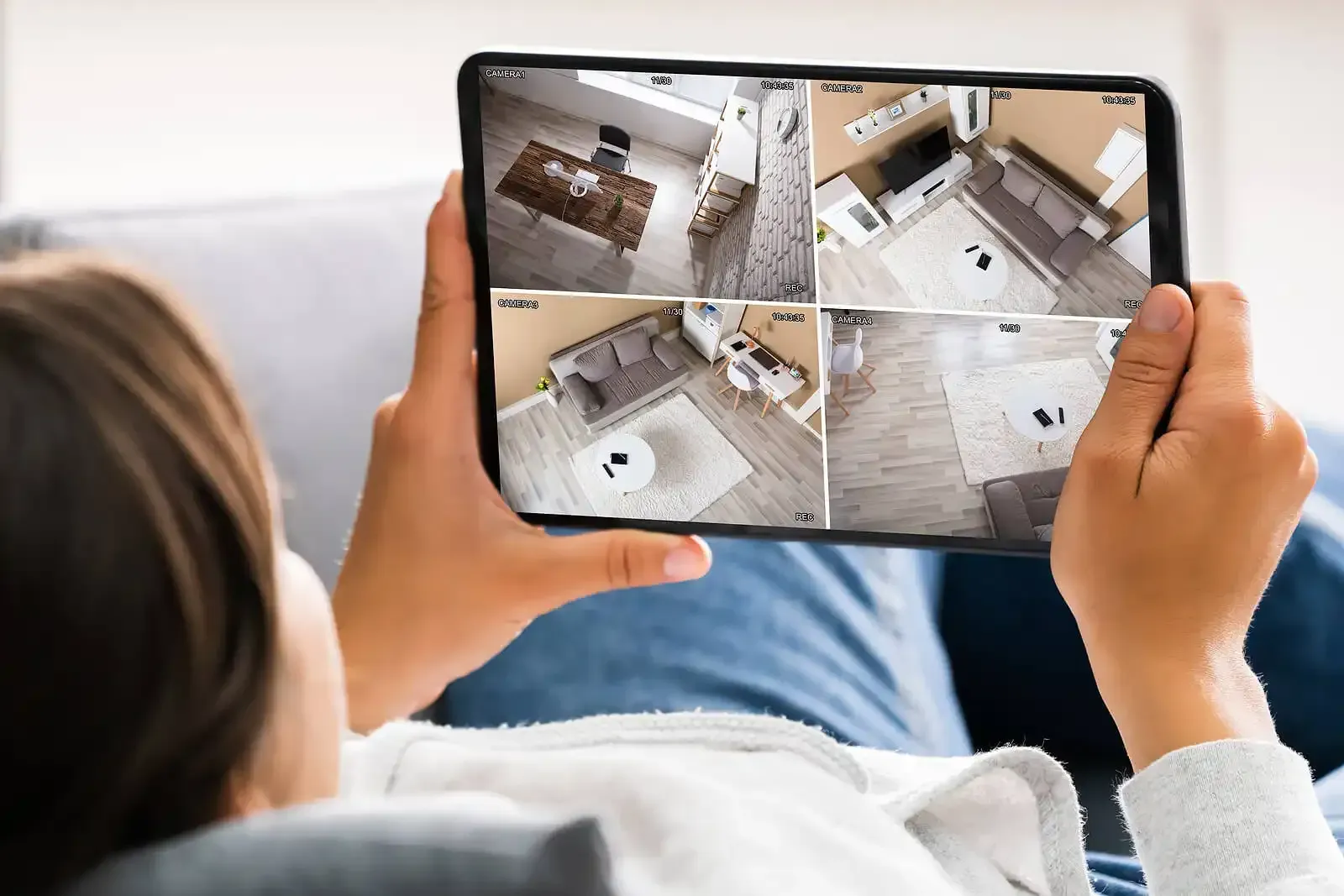 Person viewing live security camera feeds on a tablet while relaxing on a couch.